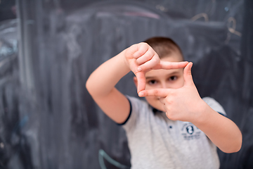 Image showing happy boy making hand frame gesture in front of chalkboard