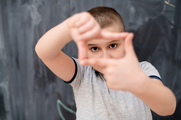 Image showing happy boy making hand frame gesture in front of chalkboard