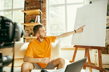 Image showing Caucasian male blogger with camera recording video review of gadgets at home