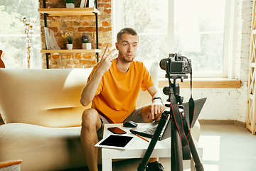 Image showing Caucasian male blogger with camera recording video review of gadgets at home