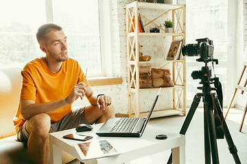 Image showing Caucasian male blogger with camera recording video review of gadgets at home