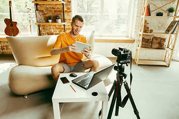 Image showing Caucasian male blogger with camera recording video review of gadgets at home