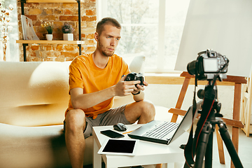 Image showing Caucasian male blogger with camera recording video review of gadgets at home