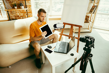 Image showing Caucasian male blogger with camera recording video review of gadgets at home