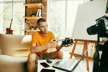 Image showing Caucasian male blogger with camera recording video review of gadgets at home