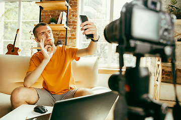 Image showing Caucasian male blogger with camera recording video review of gadgets at home