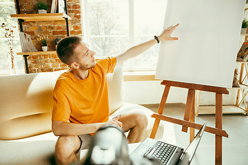 Image showing Caucasian male blogger with camera recording video review of gadgets at home