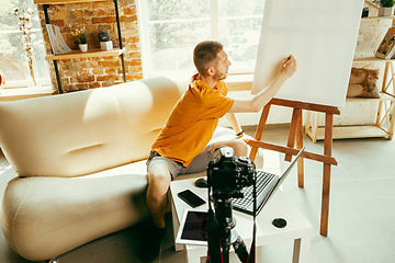 Image showing Caucasian male blogger with camera recording video review of gadgets at home