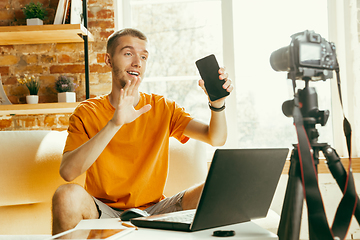 Image showing Caucasian male blogger with camera recording video review of gadgets at home