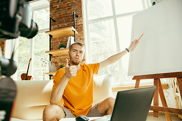 Image showing Caucasian male blogger with camera recording video review of gadgets at home