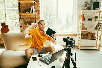 Image showing Caucasian male blogger with camera recording video review of gadgets at home