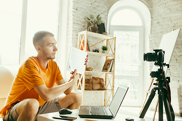 Image showing Caucasian male blogger with camera recording video review of gadgets at home