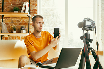 Image showing Caucasian male blogger with camera recording video review of gadgets at home