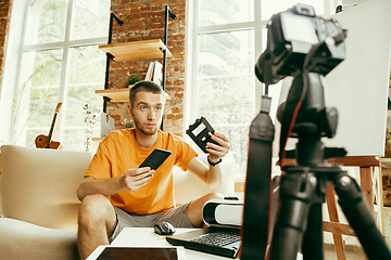 Image showing Caucasian male blogger with camera recording video review of gadgets at home