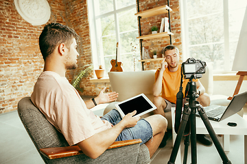 Image showing Two young male bloggers with professional camera recording video interview at home