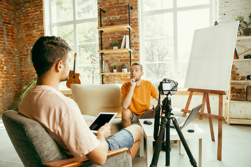 Image showing Two young male bloggers with professional camera recording video interview at home