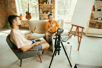 Image showing Two young male bloggers with professional camera recording video interview at home