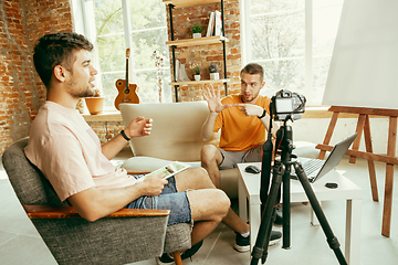 Image showing Two young male bloggers with professional camera recording video interview at home