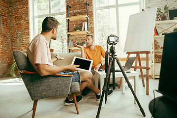 Image showing Two young male bloggers with professional camera recording video interview at home