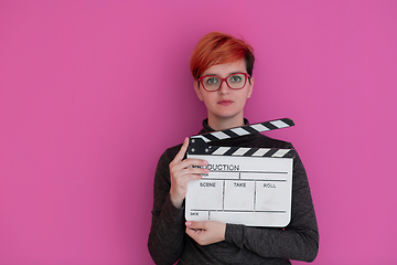 Image showing redhead woman holding movie  clapper on pink background