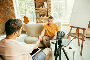 Image showing Two young male bloggers with professional camera recording video interview at home