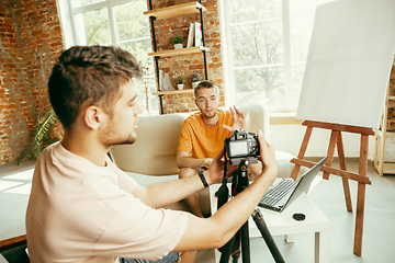 Image showing Two young male bloggers with professional camera recording video interview at home