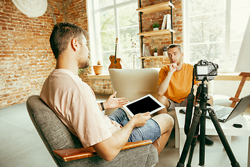 Image showing Two young male bloggers with professional camera recording video interview at home