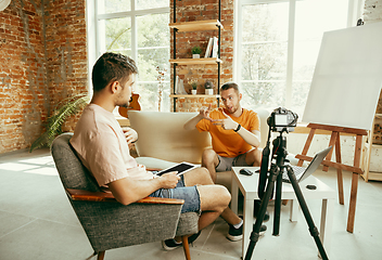 Image showing Two young male bloggers with professional camera recording video interview at home