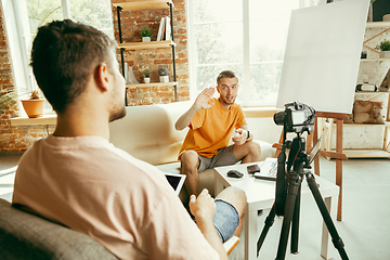 Image showing Two young male bloggers with professional camera recording video interview at home