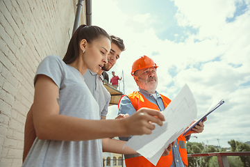 Image showing Foreman or achitect shows house, office or store design plans to a young couple