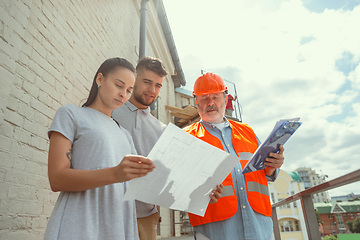 Image showing Foreman or achitect shows house, office or store design plans to a young couple