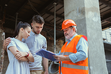 Image showing Foreman or achitect shows house, office or store design plans to a young couple