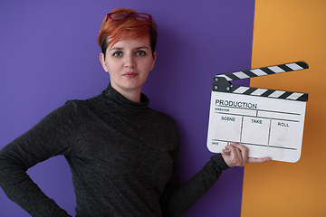 Image showing redhead woman holding movie  clapper on purple background
