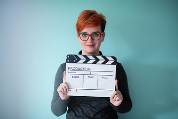 Image showing redhead woman holding movie  clapper on cyan background