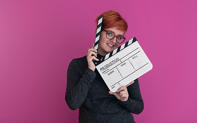 Image showing redhead woman holding movie  clapper on pink background