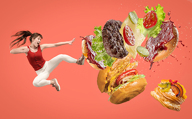 Image showing Fast food concept. Young woman fight with burger on red background