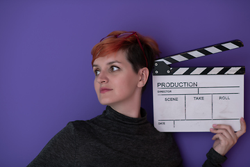 Image showing redhead woman holding movie  clapper on purple background