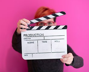 Image showing redhead woman holding movie  clapper on pink background