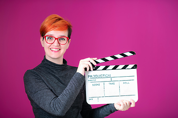 Image showing redhead woman holding movie  clapper on pink background