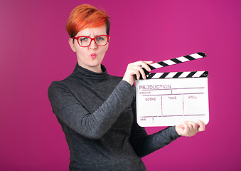 Image showing redhead woman holding movie  clapper on pink background