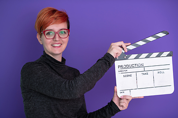 Image showing redhead woman holding movie  clapper on purple background