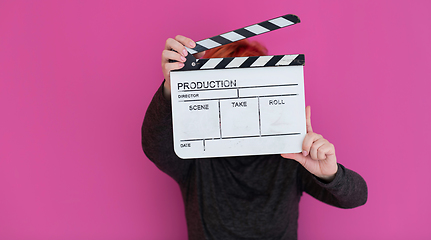 Image showing redhead woman holding movie  clapper on pink background