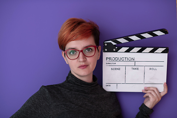 Image showing redhead woman holding movie  clapper on purple background