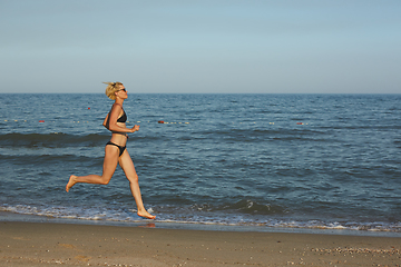 Image showing Side view of a woman running on the beach with the horizon and sea in the background