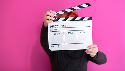 Image showing redhead woman holding movie  clapper on pink background