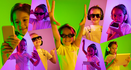 Image showing Little girl with gadgets on multicolored background in neon ligh