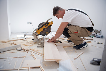 Image showing Man cutting laminate floor plank with electrical circular saw