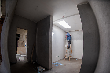 Image showing construction worker using ladder while plastering on gypsum wall