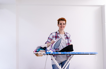 Image showing Red haired woman ironing clothes at home