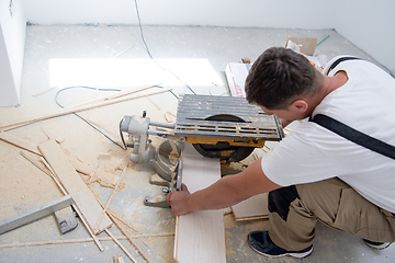 Image showing Man cutting laminate floor plank with electrical circular saw